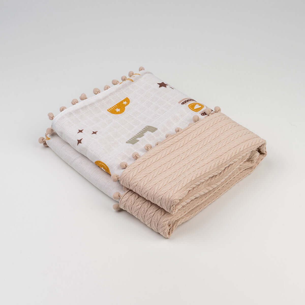 Katlanmış bej harf desenli örgü bebek battaniyesi, ponponlu